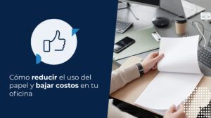 Un hombre revisando documentos de papel en una carpeta mientras trabaja en su escritorio, junto a su computadora con código en la pantalla. Esta imagen podría ilustrar cómo reducir el uso del papel en un entorno de oficina.