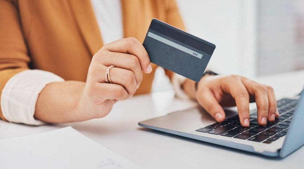 Una persona frente al computador sostiene su tarjeta de crédito en una mano, mientras con la otra concreta el proceso para comprar un certificado digital.