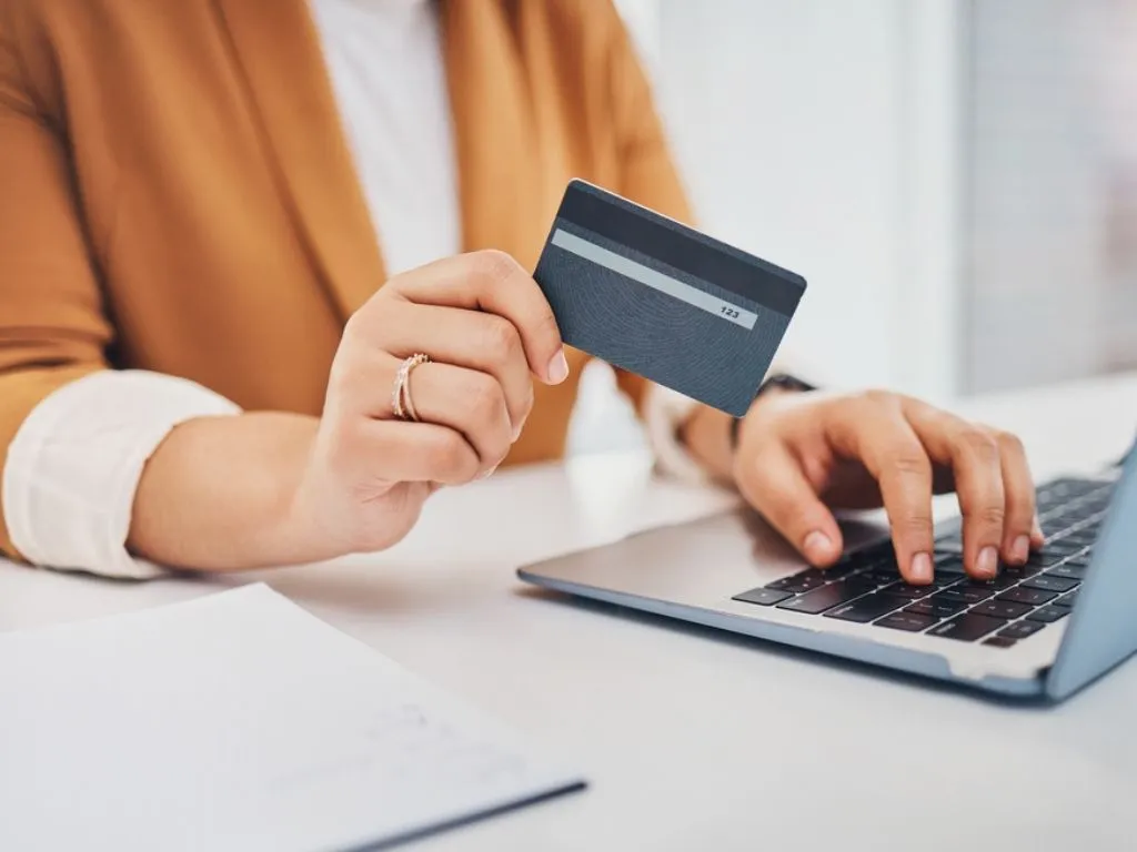 Una persona frente al computador sostiene su tarjeta de crédito en una mano, mientras con la otra concreta el proceso para comprar un certificado digital.