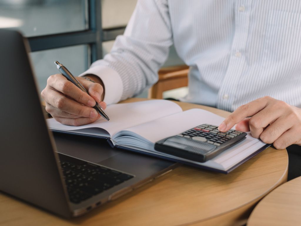 Un empresario usa una calculadora frente a un computador mientras busca cómo comprar un certificado digital para factura electrónica.