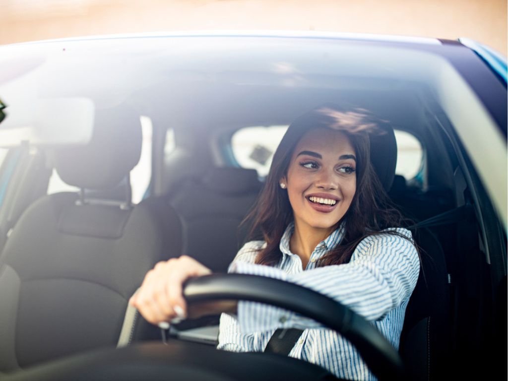 Una mujer conduce un auto y sonríe ya que obtuvo el permiso de circulación 2024.
