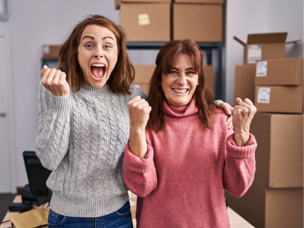 Dos mujeres celebran en su bodega al conocer los fondos para emprendedores disponibles en Chile.